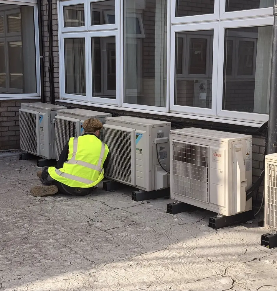 Optimal Heating & Cooling engineer servicing a row of commercial air conditioning condensers