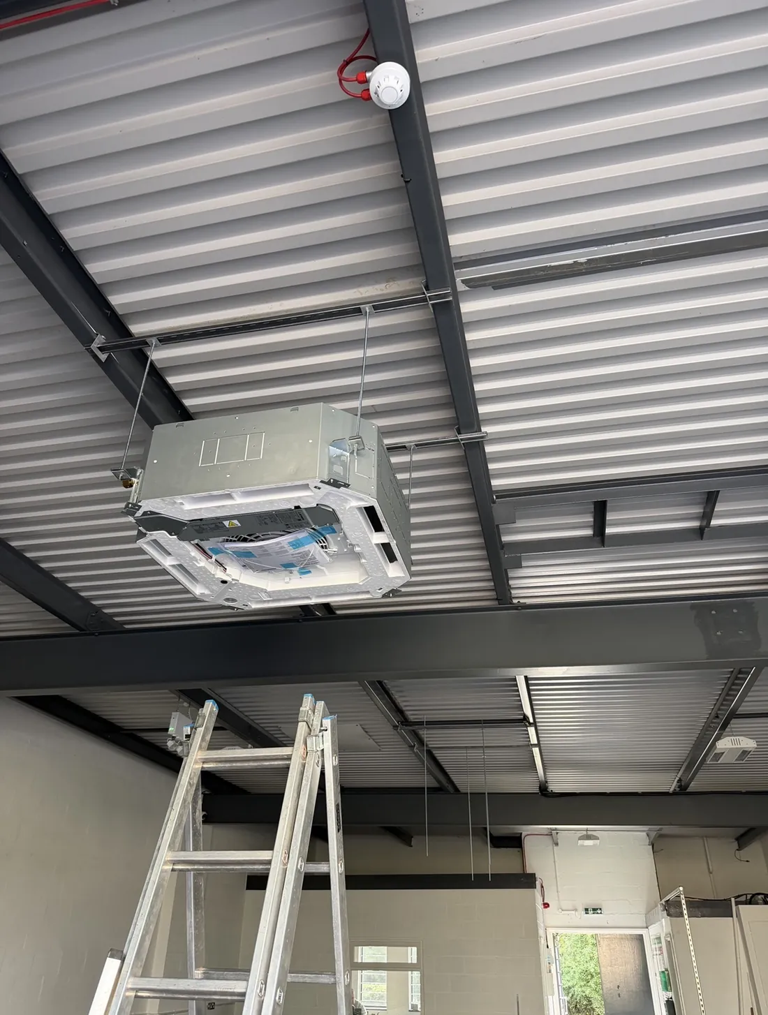 Four-way ceiling cassette suspended from a steel frame in a new commercial unit