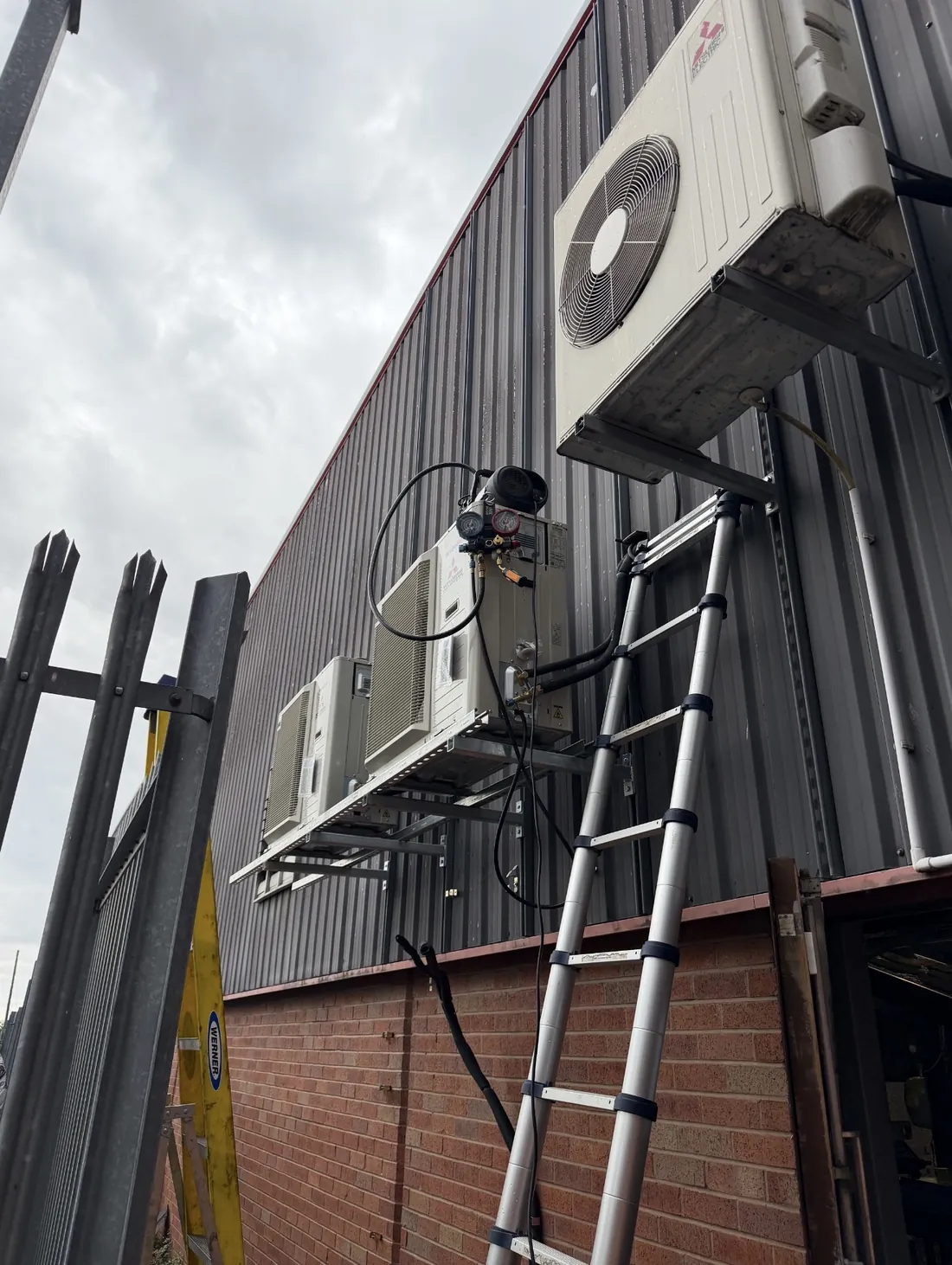 Commercial outdoor units on a wall-mounted steel platform with vacuum pump and gauges connected