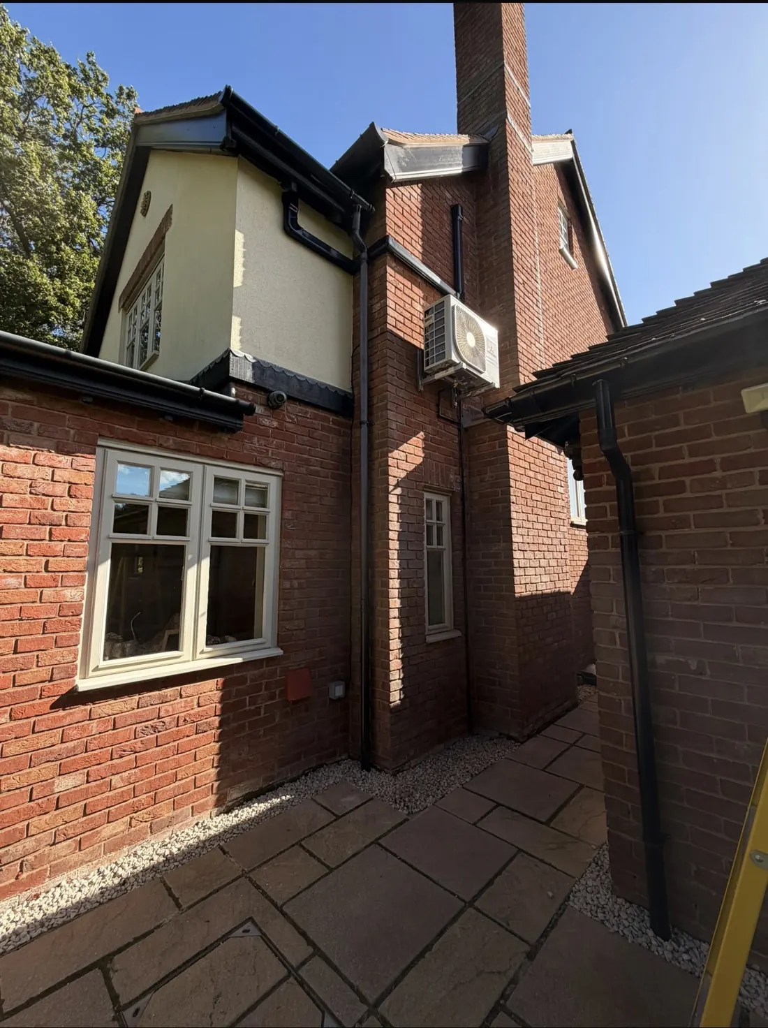 Outdoor unit on a bracket high on a red brick house with black pipework matched to the downpipes