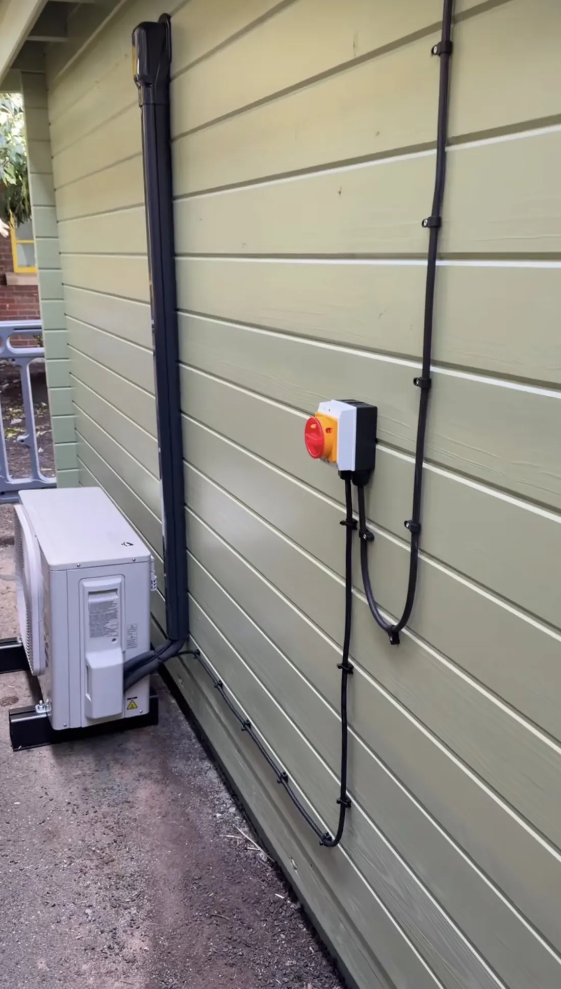 Outdoor unit with local isolator and clipped cable runs on green timber cladding