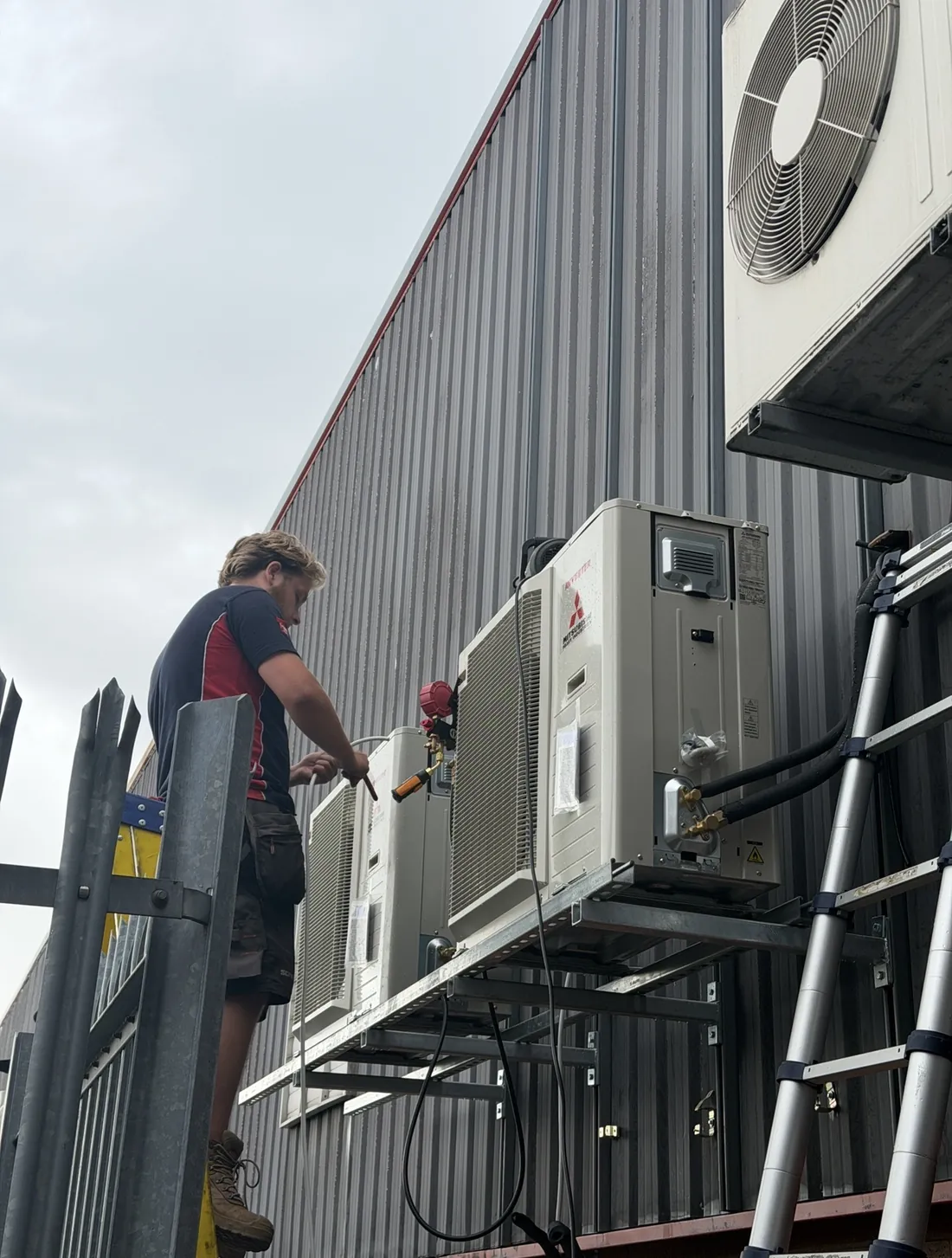 Engineer commissioning Mitsubishi Heavy Industries outdoor units on a steel platform at a commercial unit