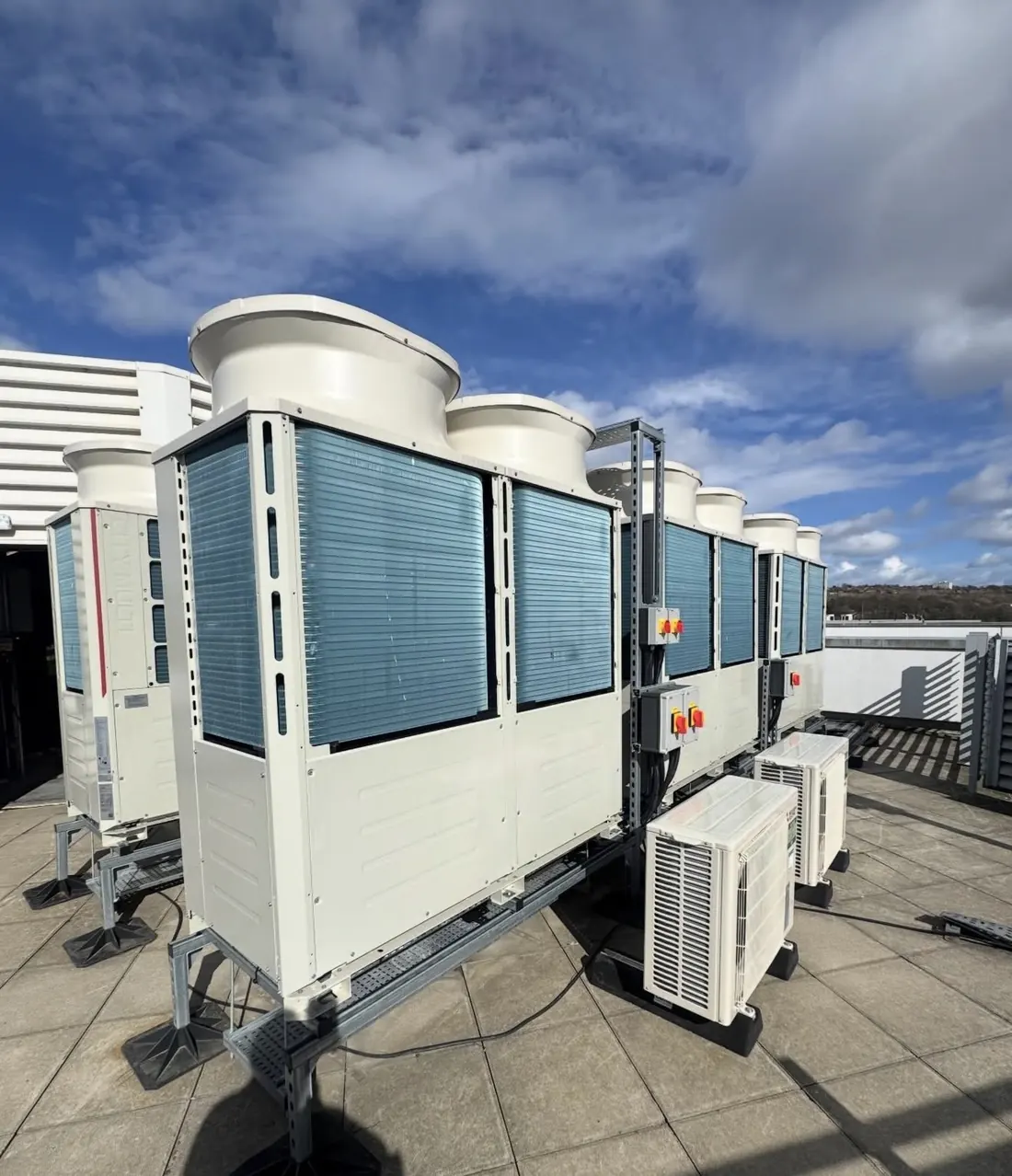 Row of VRF outdoor units on a roof frame with local isolators and a small split unit alongside