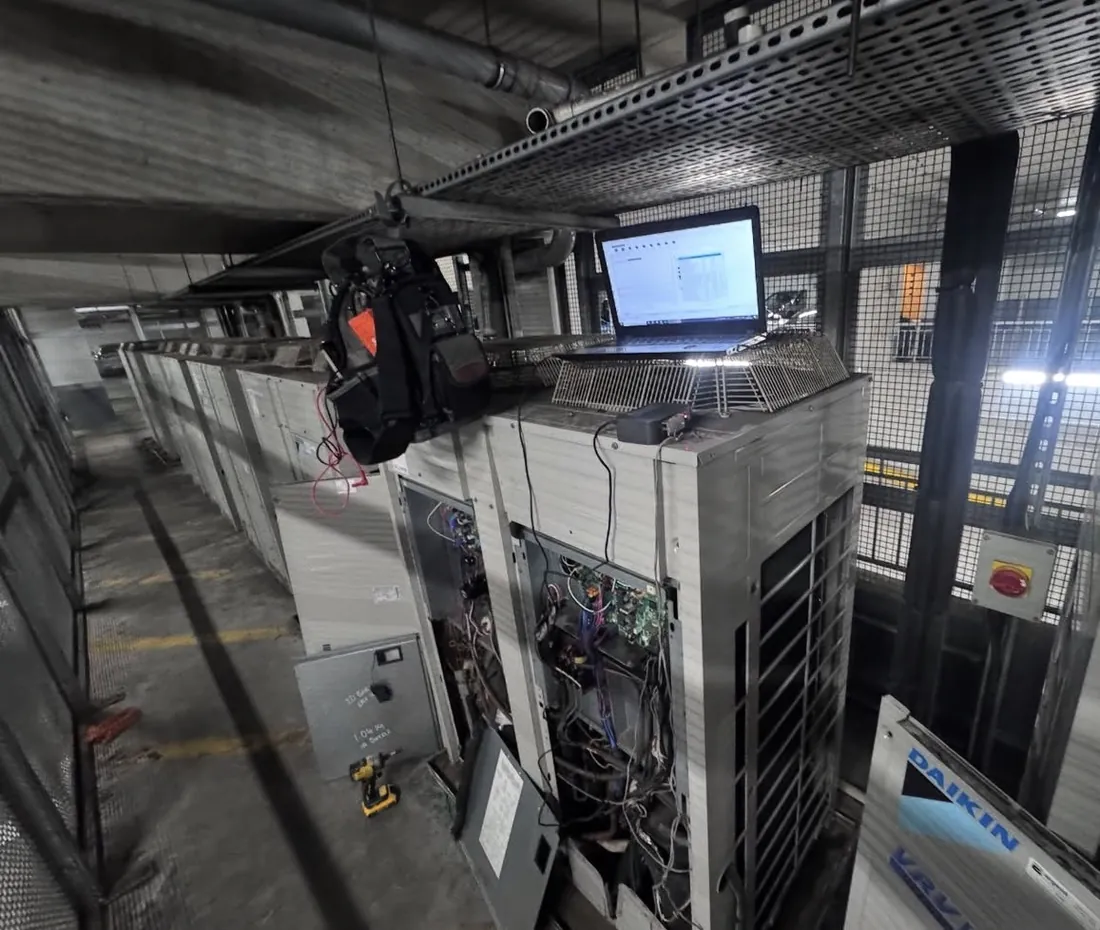 VRV outdoor units in a car park plant area with a laptop connected for commissioning and diagnostics