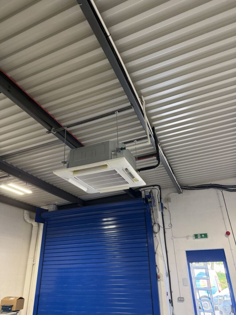 A ceiling cassette over the roller shutter, with insulated pipework and white condensate drain