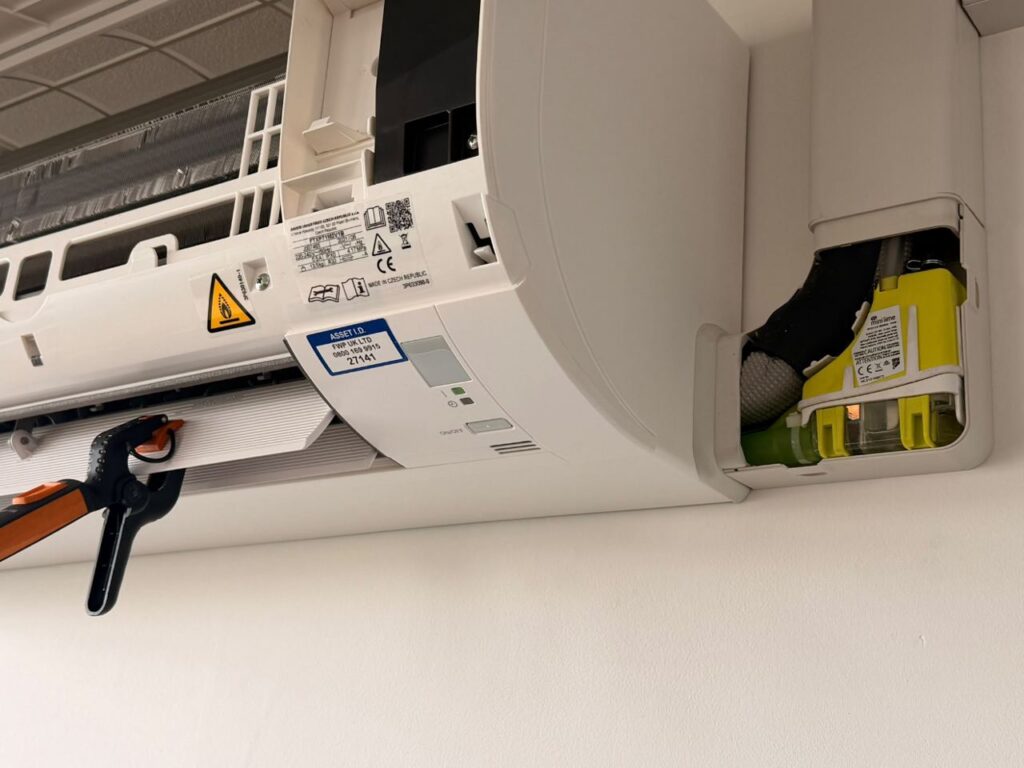 Indoor unit opened for service, showing the condensate pump and asset label